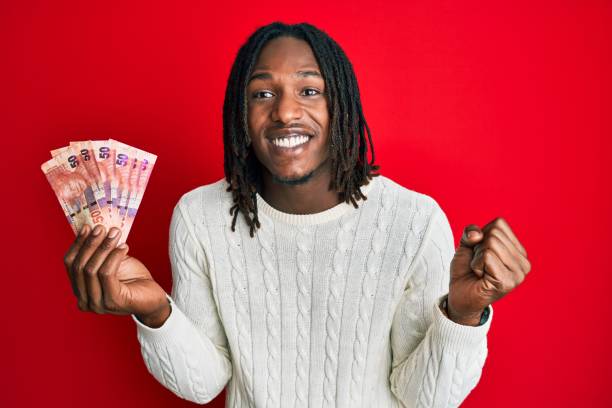 African american man with braids holding south african 50 rand banknotes screaming proud, celebrating victory and success very excited with raised arm African american man with braids holding south african 50 rand banknotes screaming proud, celebrating victory and success very excited with raised arm african currency stock pictures, royalty-free photos & images