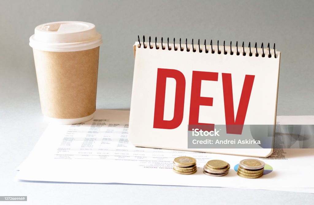 Hand with red pen. Cofee cup. Stick. Keyboard and white background. DEV sign in the notepad Abstract Stock Photo