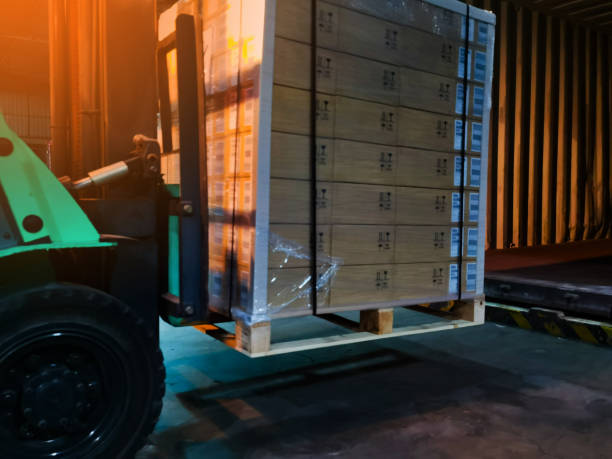 Worker driving forklift loading shipment carton boxes goods on wooden pallet at loading dock from container truck to warehouse cargo storage in freight logistics, transportation industrial, delivery trabajador conduciendo carretilla elevadora de carga cajas de cartón de mercancías en palet de madera en el muelle de carga desde el camión contenedor hasta el almacenamiento de carga de almacén en logística de carga, transporte industrial, entrega