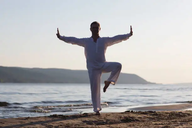 Photo of man praticing tai chi chuan at sunset on the beach. Chinese management skill Qi's energy. solo outdoor activities. Social Distancing