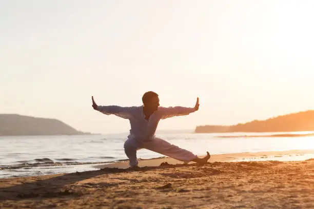 Photo of man praticing tai chi chuan at sunset on the beach. Chinese management skill Qi's energy. solo outdoor activities. Social Distancing