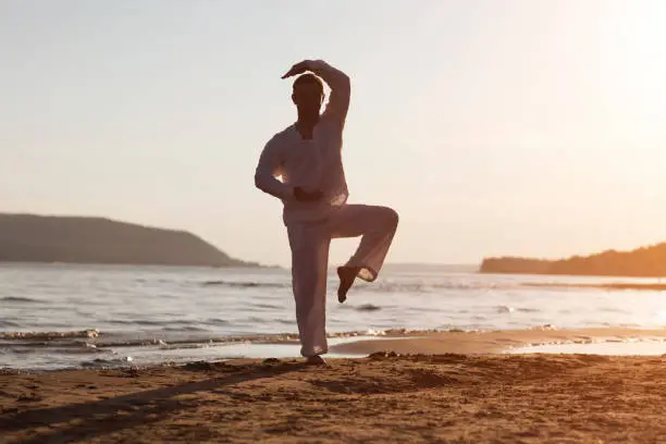 Photo of man praticing tai chi chuan at sunset on the beach. Chinese management skill Qi's energy. solo outdoor activities. Social Distancing