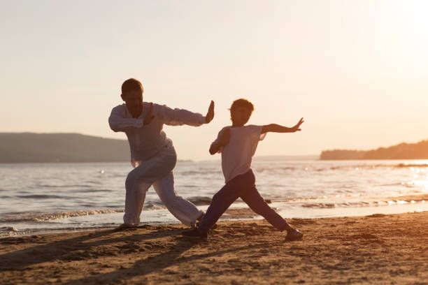 Family  dad and  son preschool child practice Tai Chi Chuan in the summer on the beach.  Chinese management skill Qi's energy. solo outdoor activities. Social Distancing. family exercising  together stock photo