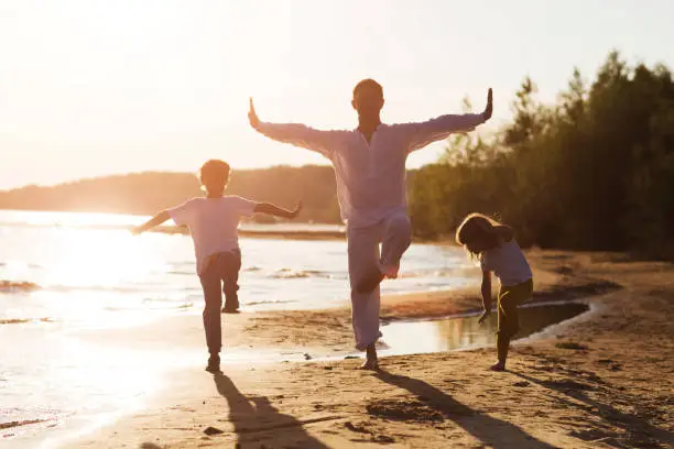 Photo of Family  dad and two kids practice Tai Chi Chuan in the summer on the beach. solo outdoor activities. Social Distancing. family exercising  together