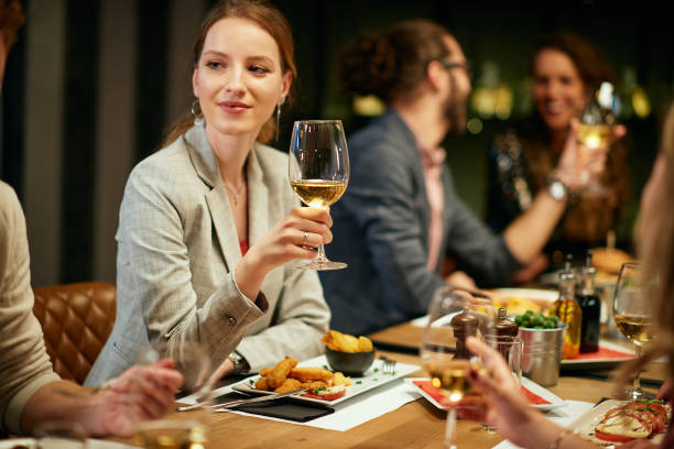 hermosa mujer sentada en el restaurante con amigos y sosteniendo una copa de vino blanco. - restaurant dinner dining gourmet fotografías e imágenes de stock