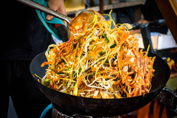 man cooking chicken pad thai on market stall - pad thai imagens e fotografias de stock