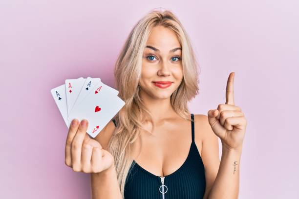 beautiful caucasian blonde girl holding ace poker cards smiling with an idea or question pointing finger with happy face, number one - smiling casino human hand beautiful imagens e fotografias de stock