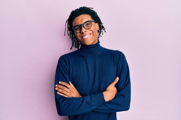 joven hombre afroamericano que lleva suéter de cuello alto y gafas de rostro feliz sonriendo con los brazos cruzados mirando a la cámara. persona positiva. - cardigan men african ethnicity african descent fotografías e imágenes de stock