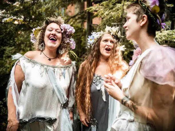 Group of women dressed in fairy costumes singing together.  Exterior of beautiful back yard garden.