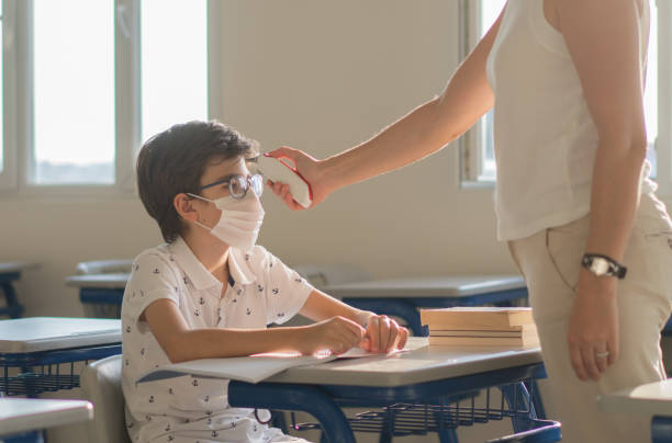 istock Teacher checks Schoolboy body temperature using infrared forehead thermometer for virus symptom - epidemic outbreak concept. 1272674049
