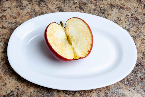 A cut red apple with a darkened and withered cut on a white plate