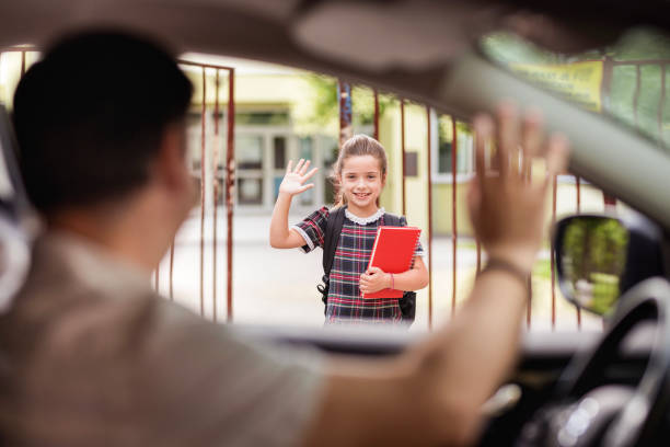 chica de pie frente al patio de la escuela y saludando a su padre pasando en un coche - car for sale fotografías e imágenes de stock
