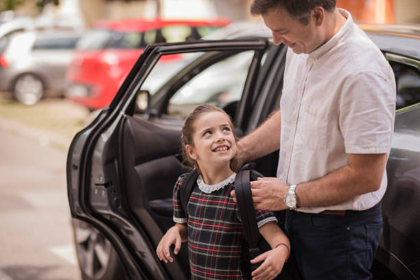 Happy young school girl looking at her dad helping her adjust school bag on her back