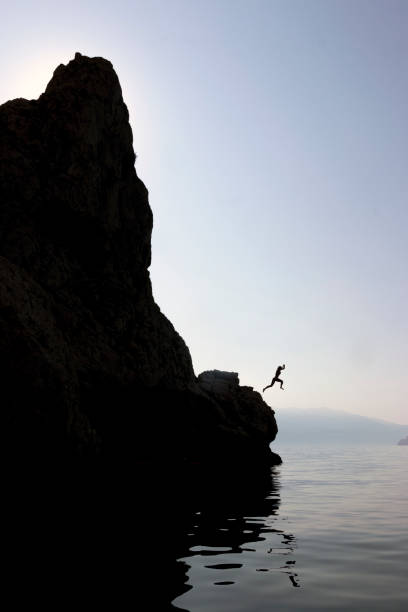 istock Woman jumping from a cliff into the sea 1272681521