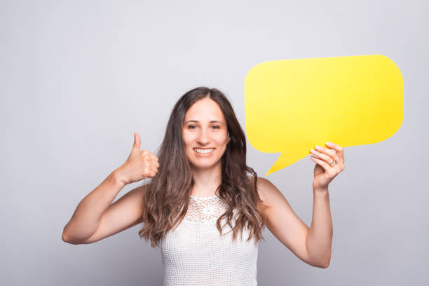 istock charming beautiful young woman showing thumb up gesture and holding empty blank speech bubble 1272682272
