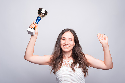 Cheerful young woman holding cup award, celebrating success.