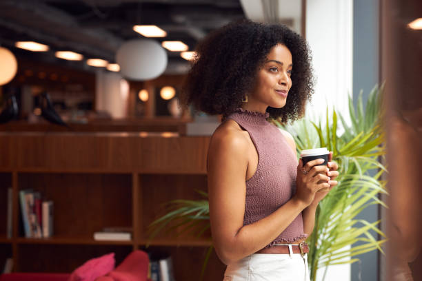 istock Young Businesswoman By Window With Takeaway Coffee Taking A Break In Modern Open Plan Office 1272683691