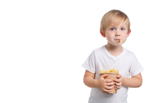 blond, białoskóre dziecko trzyma jednorazowy kubek frytek i kawałek fast foodów z jego ust. szczęśliwy chłopiec w studio strzał. - breakfast prepared potato food studio shot zdjęcia i obrazy z banku zdjęć