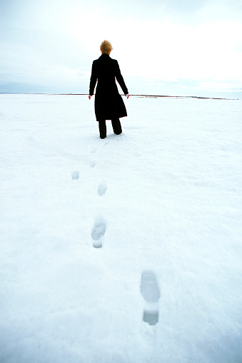 Rear view of woman walking in snow with wind swept hair.