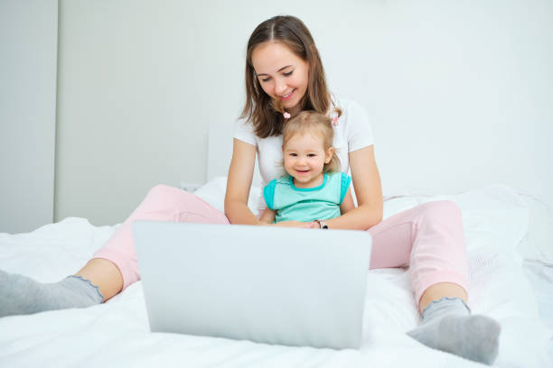 istock Caucasian toddler playing on laptop with mom while sitting on bed 1272692938