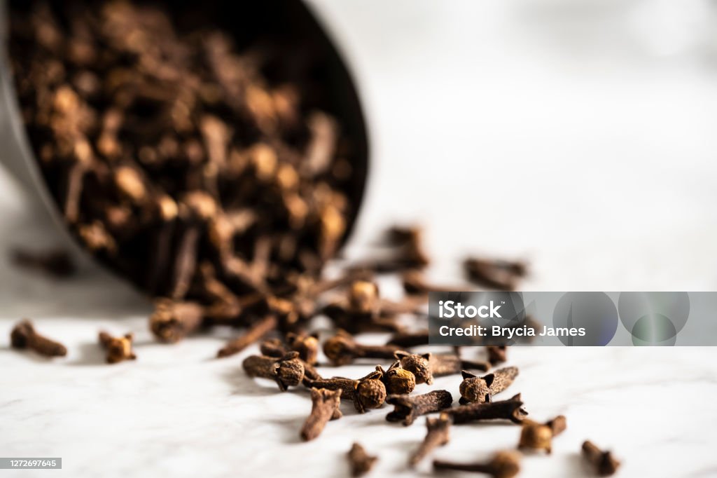 Scoop of Cloves on a White Marble Surface A scoop full of cloves dumping out on a white marble surface. Clove - Spice Stock Photo