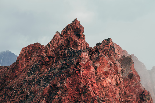 Surreal pointed rocky pinnacle in cloudy sky. Vivid big pointy rocky peak. Giant piece of stone. Atmospheric minimalist alpine landscape. Sharp rocky mountain top in sky. Wonderful highland scenery.