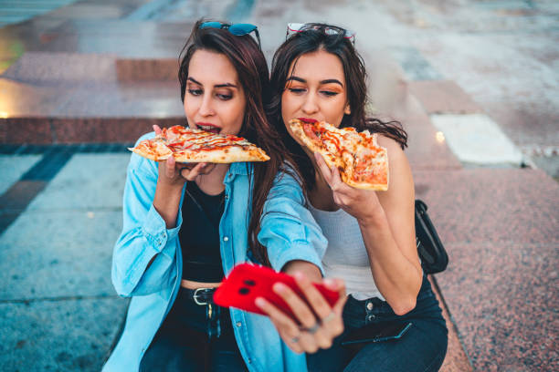 istock Two young women eating pizza and making selfie 1272705909