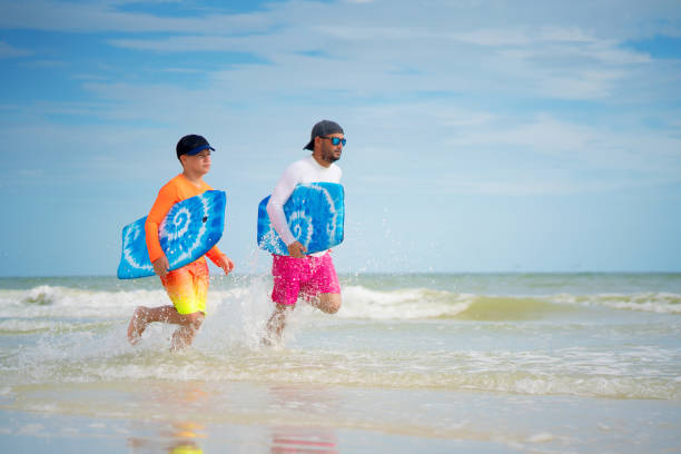 istock Father and son running with skimboards on shallow waters 1272709282
