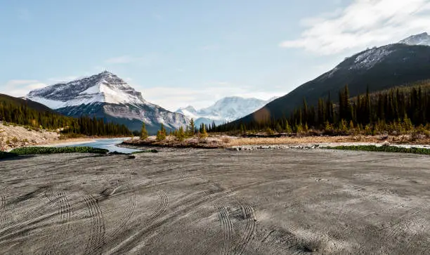 Photo of empty dirt beach with traces against Canadian Rockies