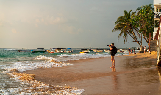 The mature woman, the traveler, and photographer shooting on the beach in Hikkaduwa, Sri Lanka.