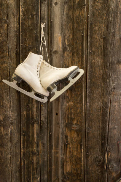 Figure skates hanging frm an old fashioned coat peg on a red wall background.