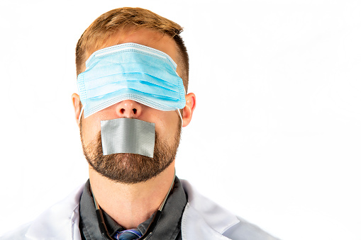 A studio depiction of a male doctor blindfolded by a surgical mask with duct tape across his mouth.