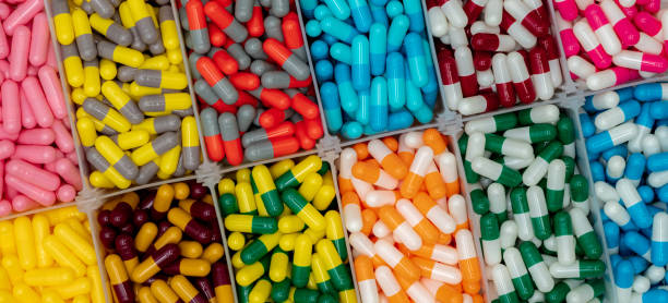 píldoras cápsula de colores en caja de plástico. industria farmacéutica. píldoras de cápsulas rosas, amarillas, azules, verdes, naranjas, grises, rojas y blancas. asistencia sanitaria y medicina. concepto de vitaminas y suplementos. - amoxicillin fotografías e imágenes de stock