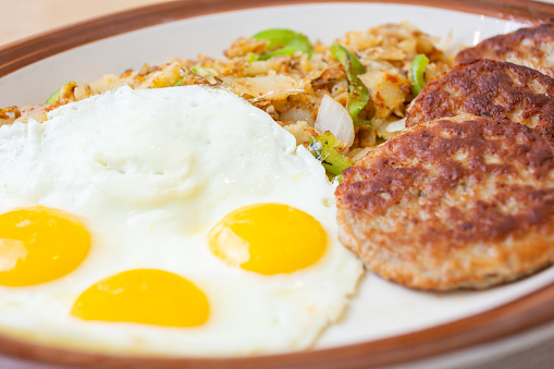 A closeup view of a breakfast plate featuring eggs, sausage patties and home fries, in a restaurant or kitchen setting.