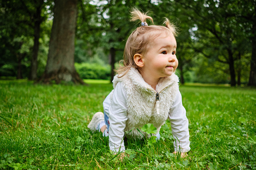 A joyful child crawls the grass in the park.