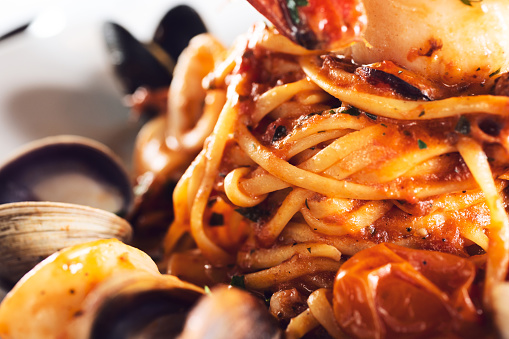 A closeup view of a twirl of tagliolini with an array of seafood, in a restaurant or kitchen setting.