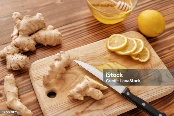 Preparation Of Cold And Flu Remedy Cure Drink Close Up Of Board Knife Fresh Ginger Lemon Honey In A Bowl With Dipper On The Wooden Table Stock Photo - Download Image Now
