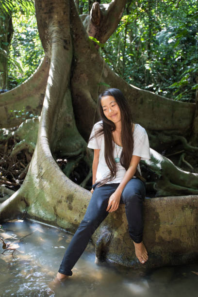 istock Okinawan girl sitting on big tree root 1272732617