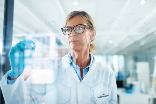 Shot of a mature scientist drawing molecular structures on a glass wall in a lab
