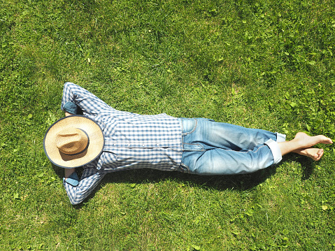 A man in sunglasses is resting in the park, lying on his back on the green grass and looking at the sky.