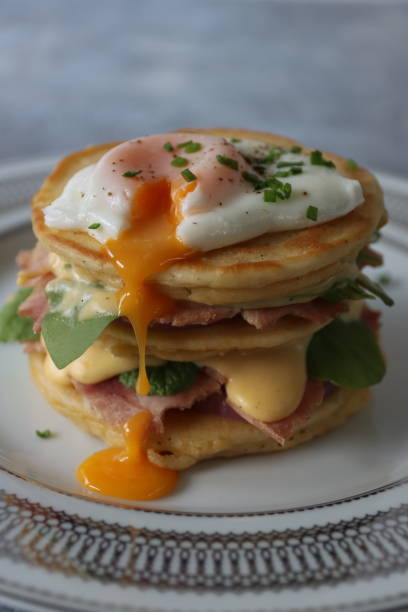 istock Image of stack of mini pancakes, florentine eggs benedict recipe, layers of pancake, bacon, spinach leaves, hollandaise sauce and poached egg with oozing egg yolk, focus on foreground 1272738535