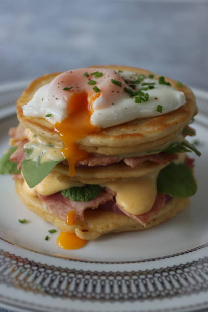 istock Image of stack of mini pancakes, florentine eggs benedict recipe, layers of pancake, bacon, spinach leaves, hollandaise sauce and poached egg with oozing egg yolk, focus on foreground 1272738547