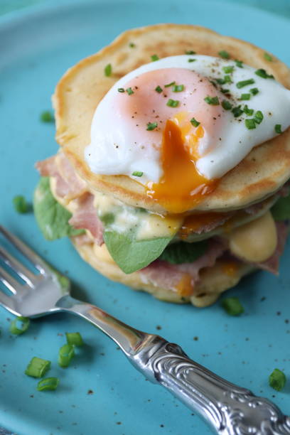 istock Full frame image of turquoise blue plate with metal fork and stack of mini pancakes, florentine eggs benedict recipe, layers of pancake, bacon, spinach leaves, hollandaise sauce and poached egg with oozing egg yolk, focus on foreground 1272738548