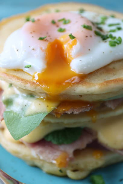 istock Full frame, close-up image of turquoise blue plate and stack of mini pancakes, florentine eggs benedict recipe, layers of pancake, bacon, spinach leaves, hollandaise sauce and poached egg with oozing egg yolk 1272738552