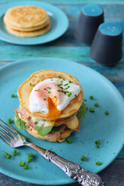 istock Image of turquoise blue plate, metal fork and stack of mini pancakes, florentine eggs benedict recipe, layers of pancake, bacon, spinach leaves, hollandaise sauce, poached egg, salt cellar, pepper pot, blue wood background, focus on foreground 1272738564