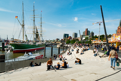 Hamburg, Germany - September 13. 2020: People enjoy the beautiful weather while strolling along the Hamburg harbor promenade and sit on the open stairs