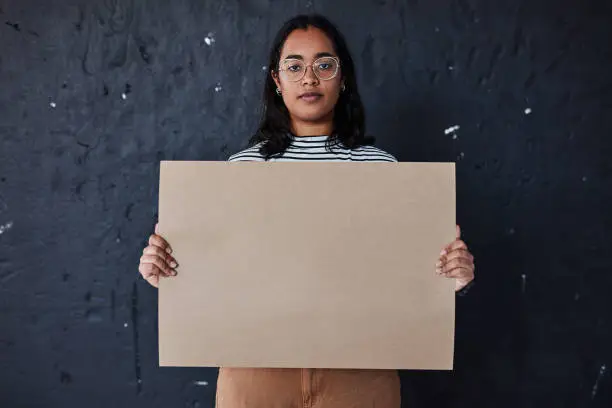 Studio shot of a young woman holding a blank poster against a dark background