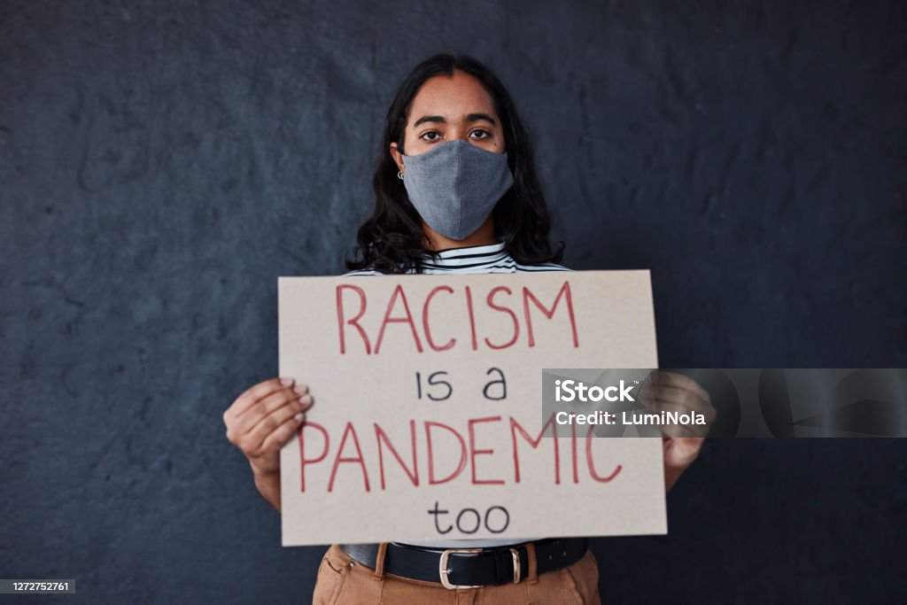 Discrimination is a real disease Studio shot of a masked young woman protesting against racism against a dark background Racism Stock Photo