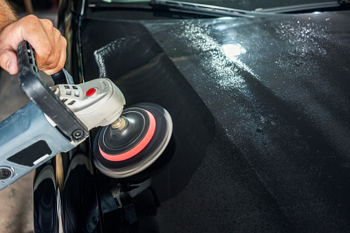 Man polishing a car segment using an electric orbital polisher in garage