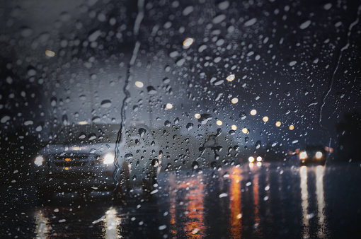 Blurry wet road with light reflections,twilight scene during hard rain fall.View through the wind shield with selective focus and color toned.